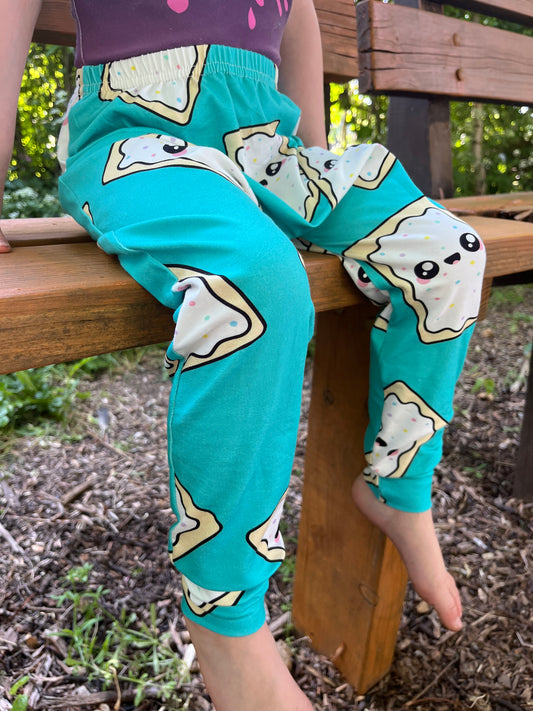 Child wearing turquoise baggy harem pants with cartoon pop-tart print and sprinkles