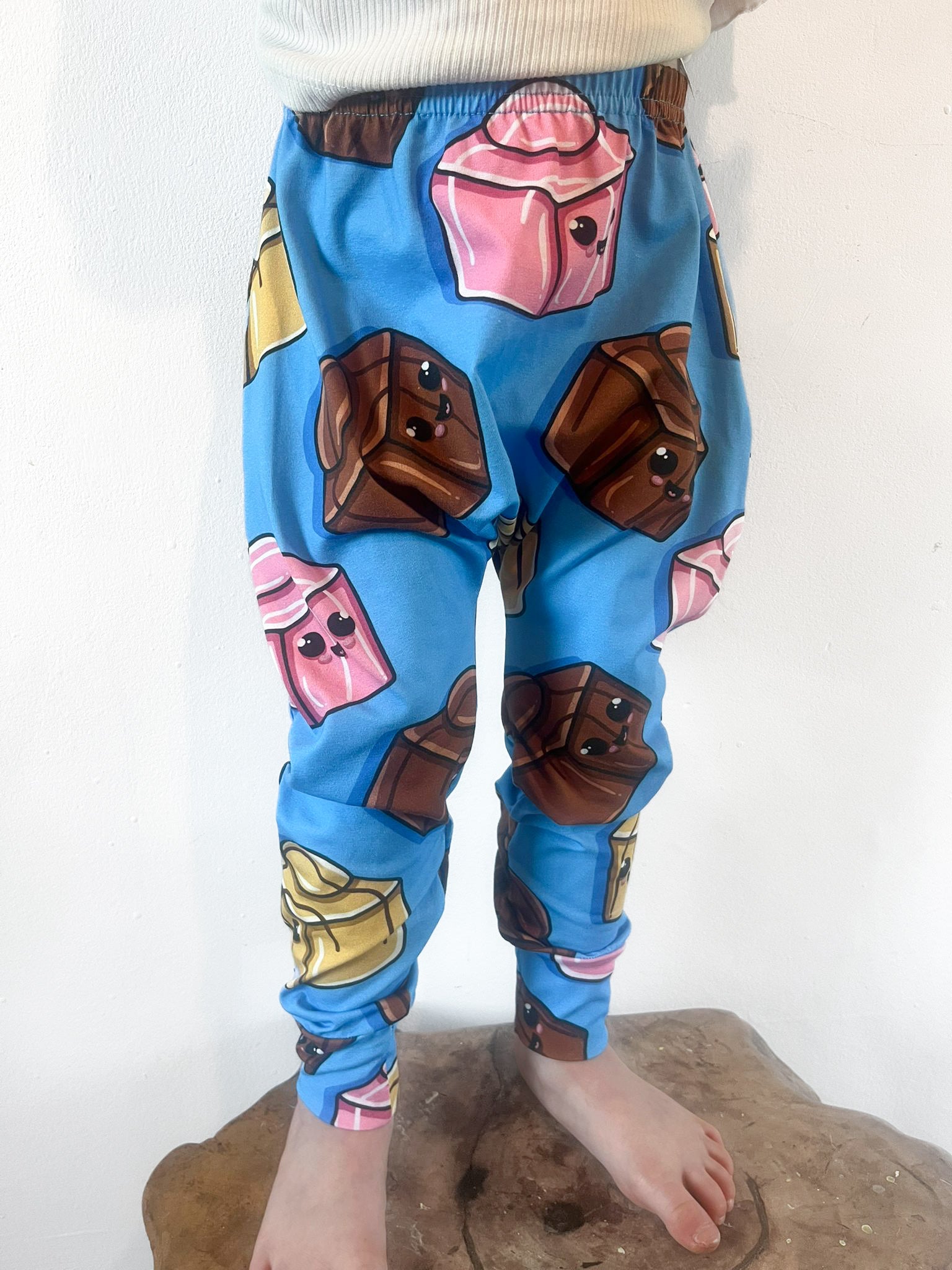 Child wearing blue harem pants with cartoon chocolate block design featuring pink, brown and gold sweets