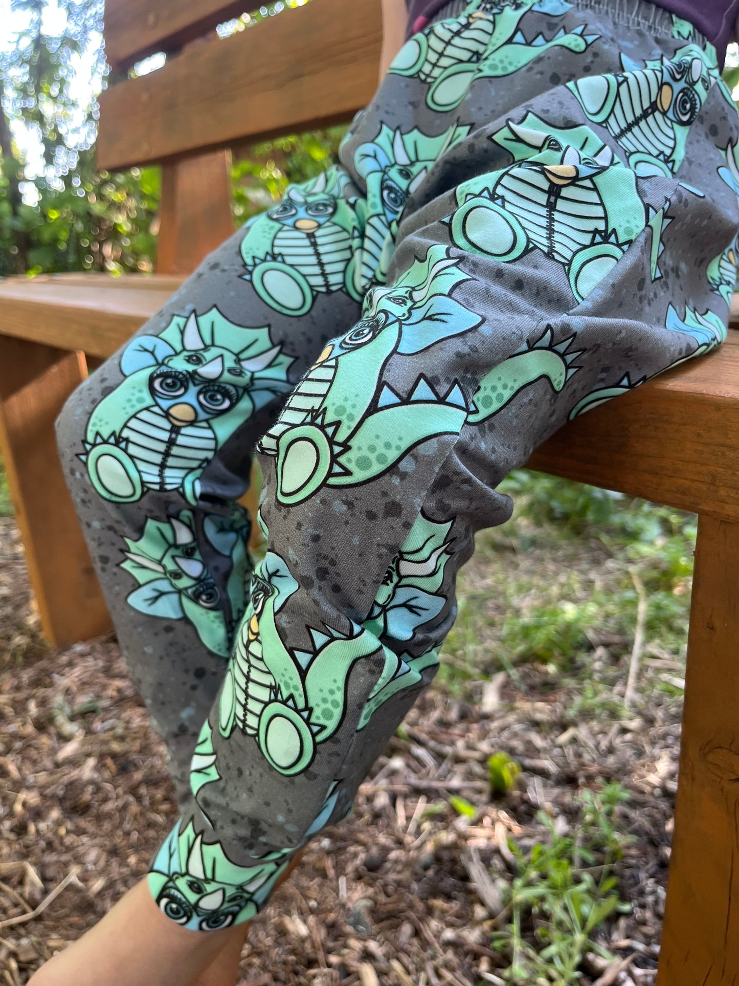 Child wearing grey baggy harem pants with mint green triceratops dinosaur print
