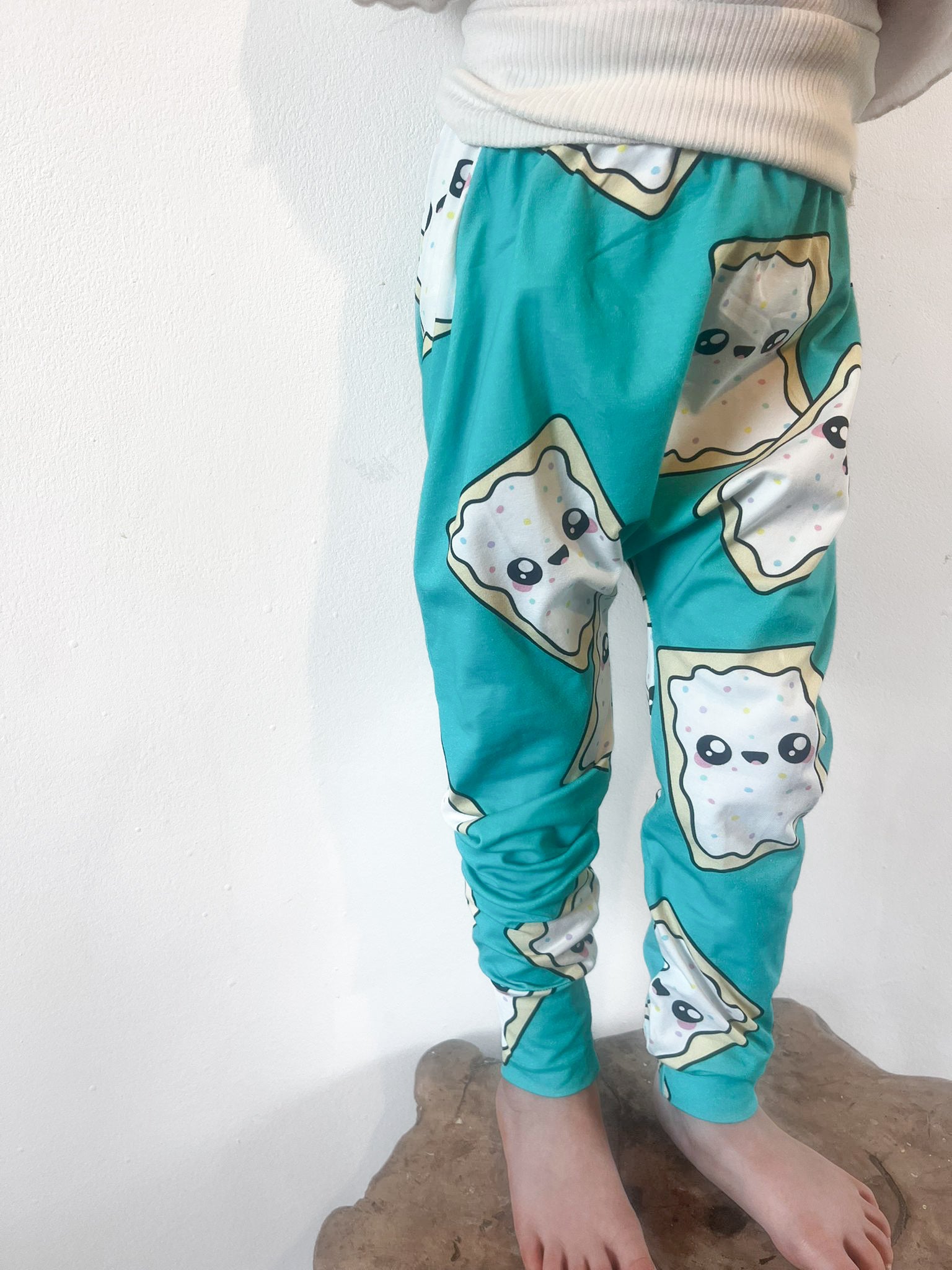 Child wearing turquoise baggy harem pants with cartoon pop-tart print and sprinkles