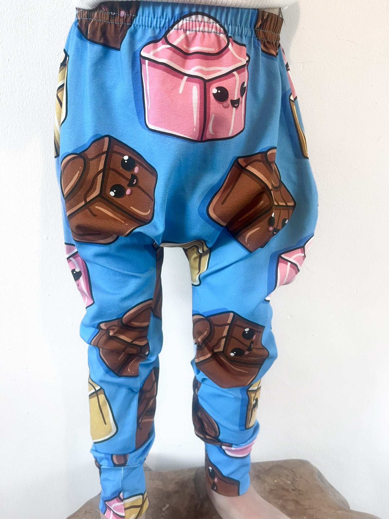 Child wearing blue harem pants with cartoon chocolate block design featuring pink, brown and gold sweets