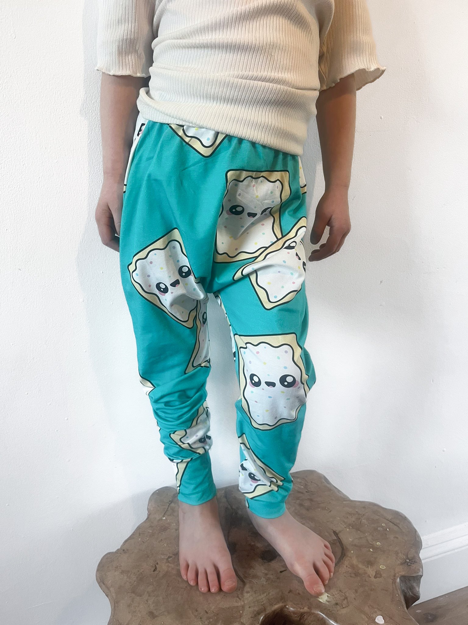 Child wearing turquoise baggy harem pants with cartoon pop-tart print and sprinkles