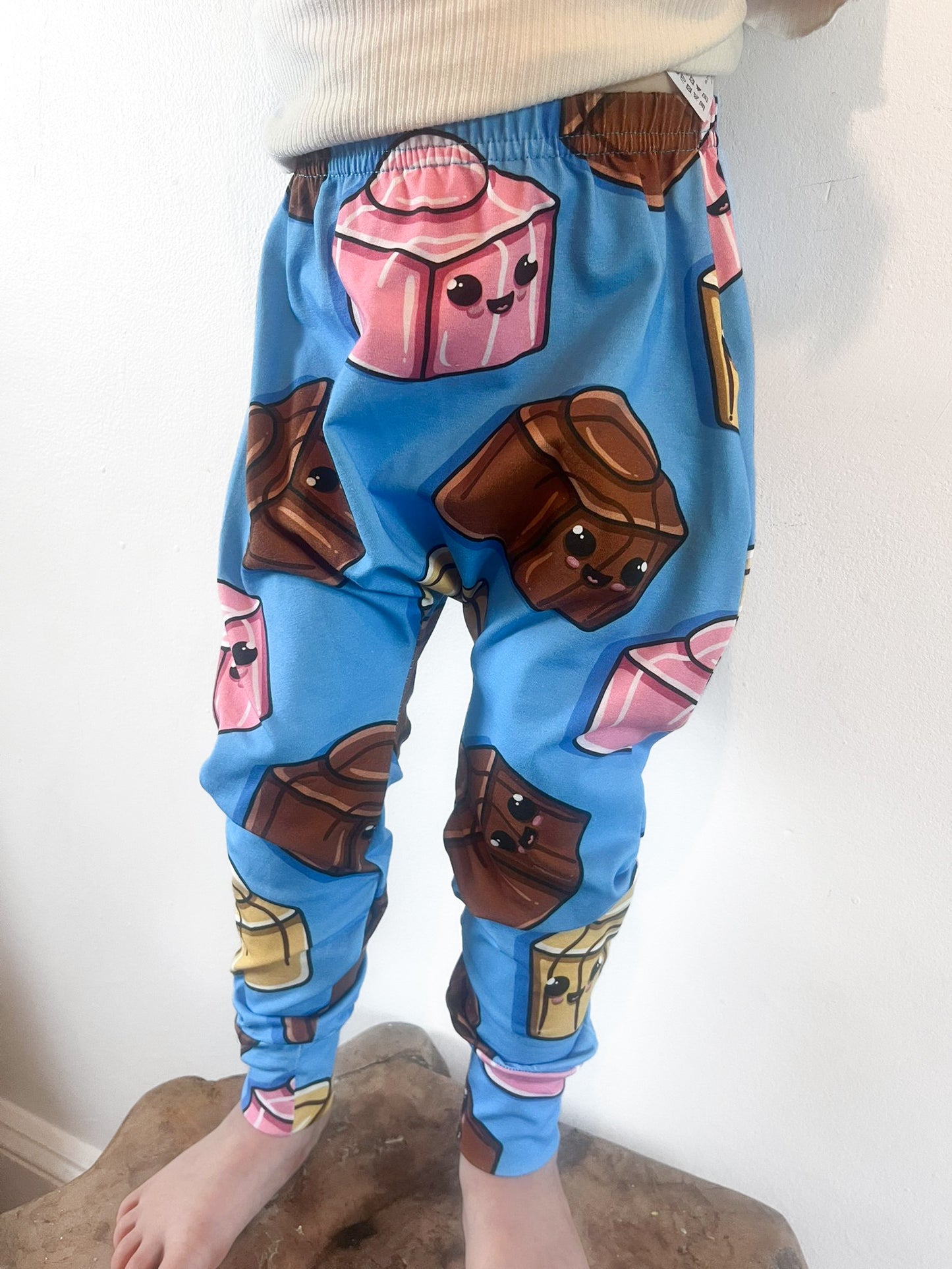 Child wearing blue harem pants with cartoon chocolate block design featuring pink, brown and gold sweets