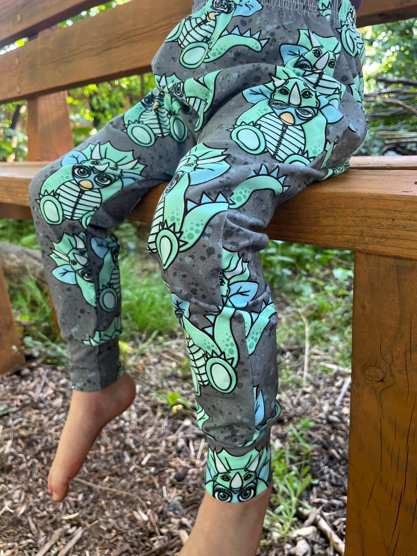 Child wearing grey baggy harem pants with mint green triceratops dinosaur print
